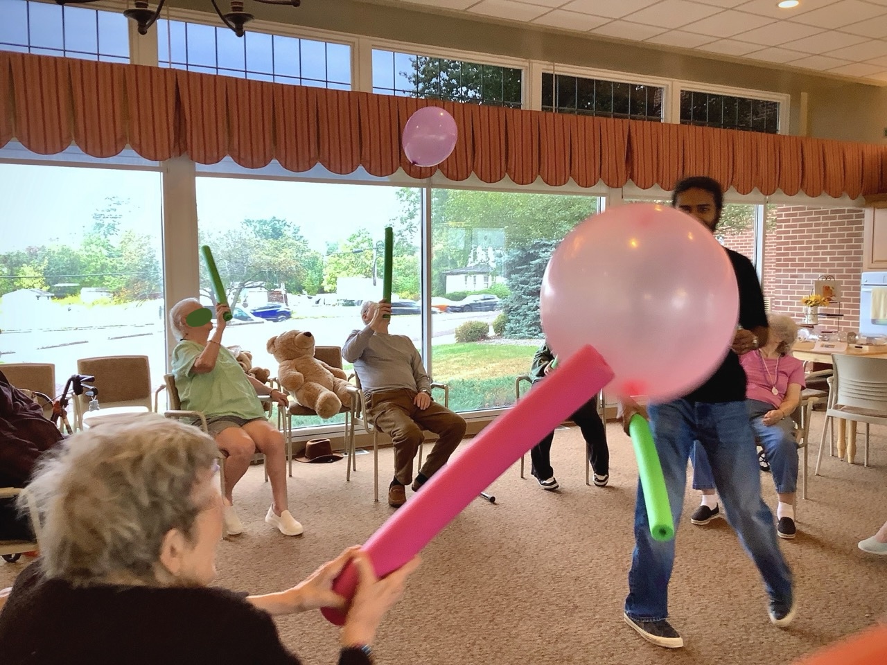 Older adults in a group session batting a balloon with pool noodles