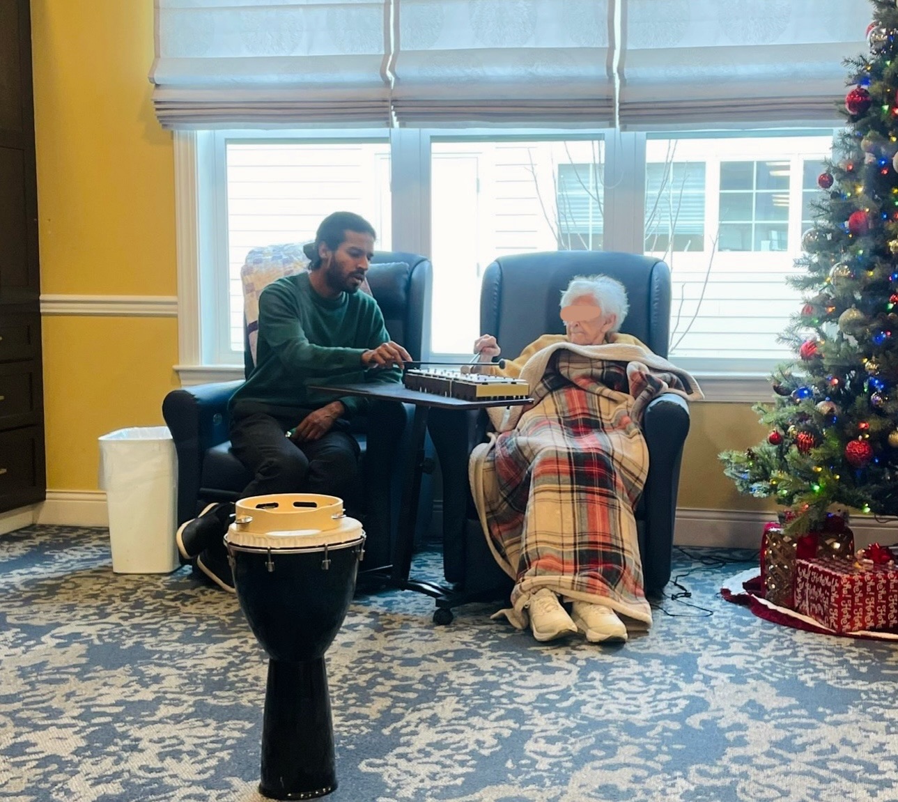 A music therapist playing a mallet instrument one-on-one with an older adult seated in a chair