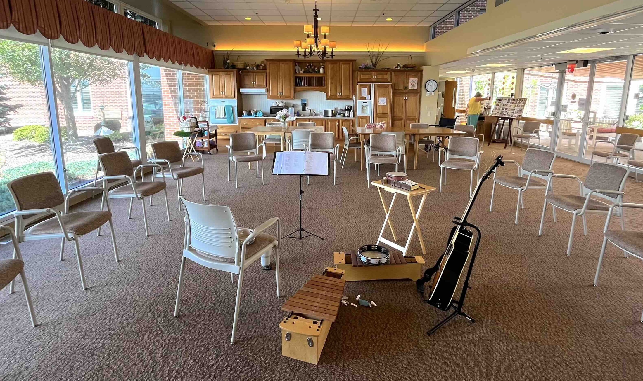 A bright community room set up for a group music session, with a circle of chairs, a guitar, and mallet instruments